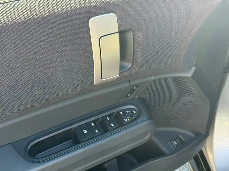 Gros plan sur la porte avant gauche argentée d'une MINI Countryman avec commandes de vitres et poignée intérieure argentée.