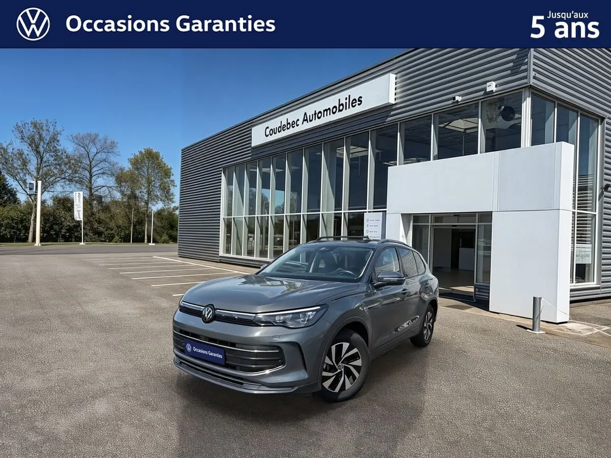 Volkswagen Tiguan gris en 3/4 avant droit, avec jantes alliage noir brillant, devant un bâtiment de concession.