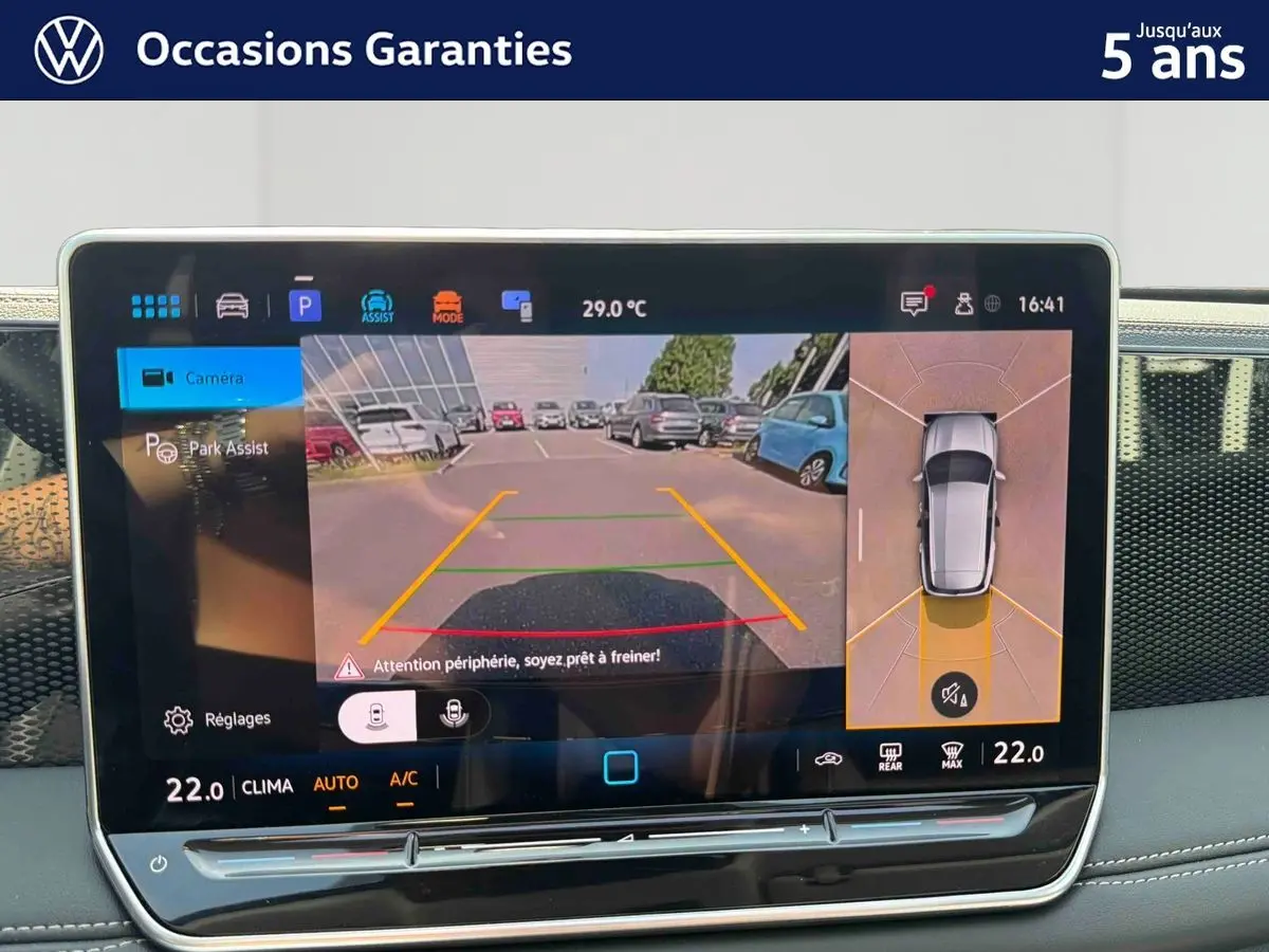 Écran tactile intérieur montrant l'aide au stationnement avec vue caméra arrière et angles morts du Volkswagen Tiguan gris.