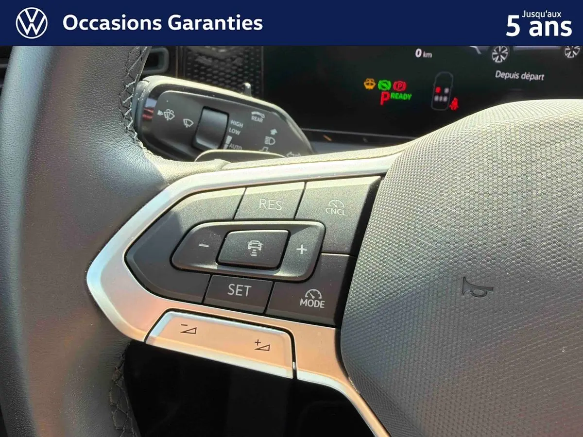 Gros plan sur le volant multifonction cuir du Volkswagen Tiguan gris, avec commandes de régulateur de vitesse visibles.