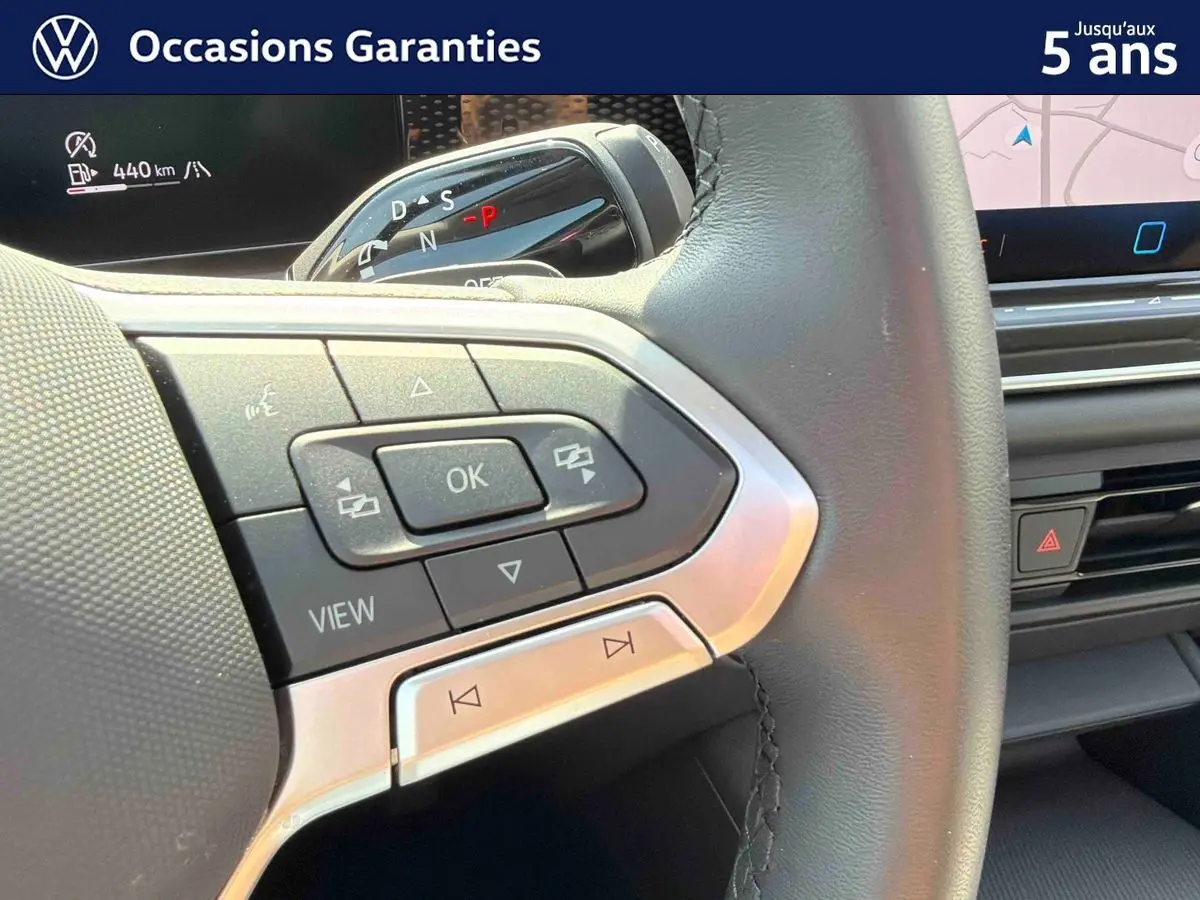 Gros plan sur les commandes multifonctions à gauche du volant cuir du Volkswagen Tiguan gris, avec écran tactile en arrière-plan.