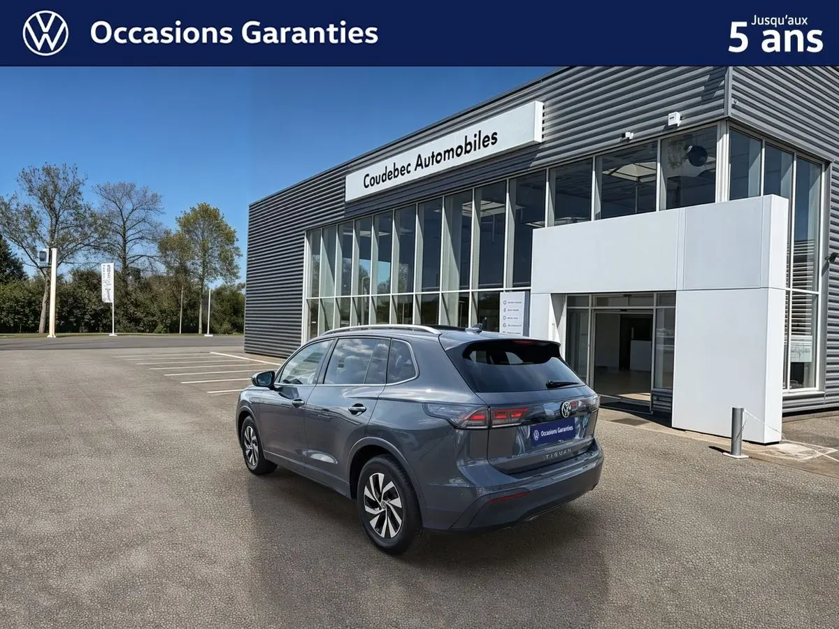 Volkswagen Tiguan gris vu en 3/4 arrière droit devant un bâtiment de concession Coudebec Automobiles.