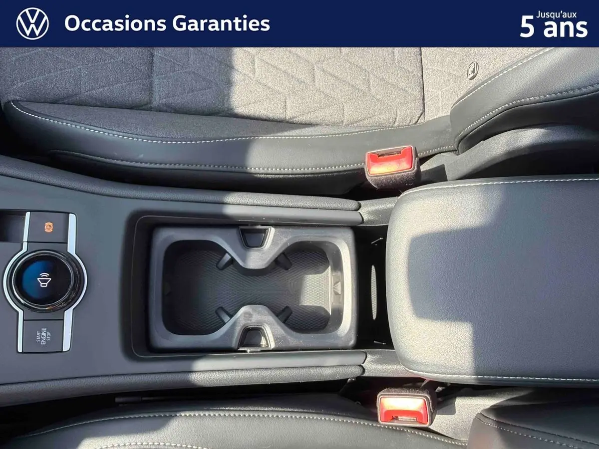 Vue plongeante sur la console centrale noire du Volkswagen Tiguan 2025, avec porte-gobelets et frein de stationnement électronique.