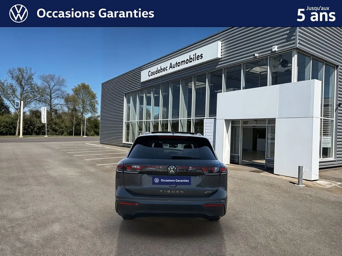 Vue arrière d’un Volkswagen Tiguan gris 2025 garé devant un bâtiment moderne avec vitres et enseigne Coudebec Automobiles.