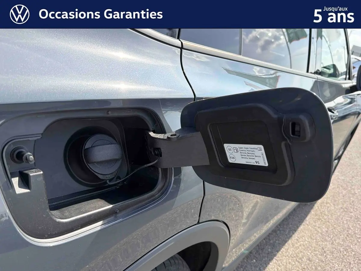 Vue rapprochée de la trappe à carburant ouverte côté gauche d’un Volkswagen Tiguan gris 2025, détails du bouchon visibles.