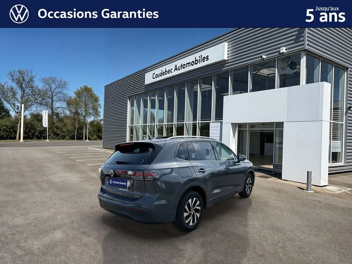 Vue 3/4 arrière droite d'un Volkswagen Tiguan gris avec jantes alliage noir devant un bâtiment moderne.