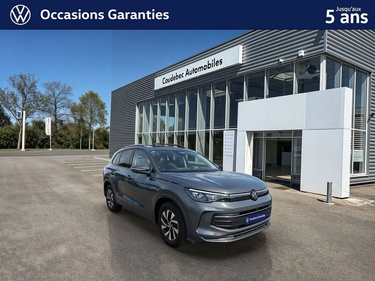 Volkswagen Tiguan gris vu en 3/4 avant droit, avec jantes alliage noir brillant, devant un showroom moderne.