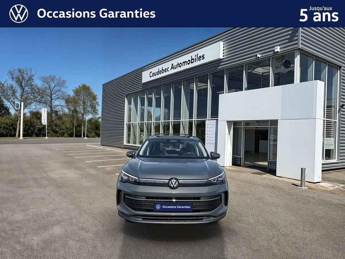 Volkswagen Tiguan gris vu de face, avec calandre épurée et phares LED, devant un bâtiment moderne de concession.