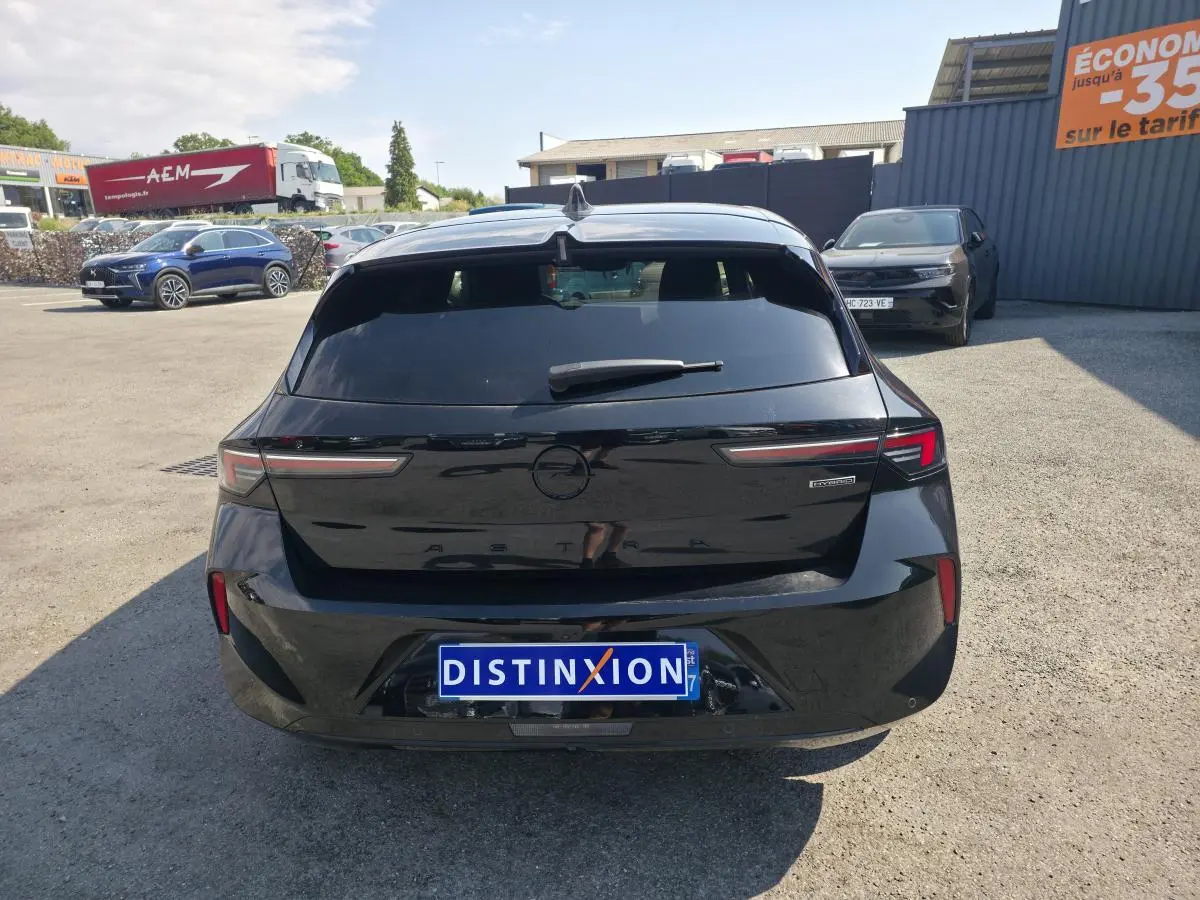 Vue arrière d'une Opel Astra Hybrid noire avec feux LED fins et logo Opel noir sur un parking extérieur.