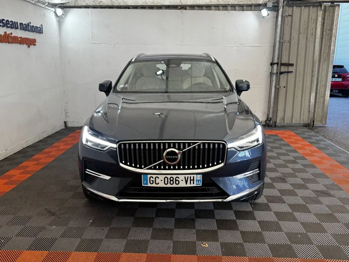 Vue frontale d'un Volvo XC60 bleu avec calandre verticale chromée et phares LED allumés dans un garage.