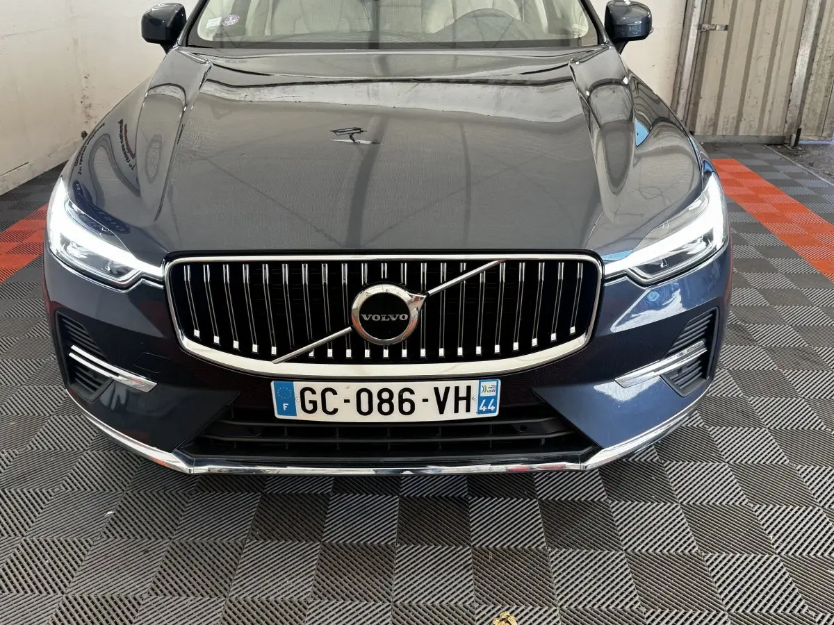 Vue avant rapprochée du Volvo XC60 bleu avec calandre verticale chromée et phares LED allumés.