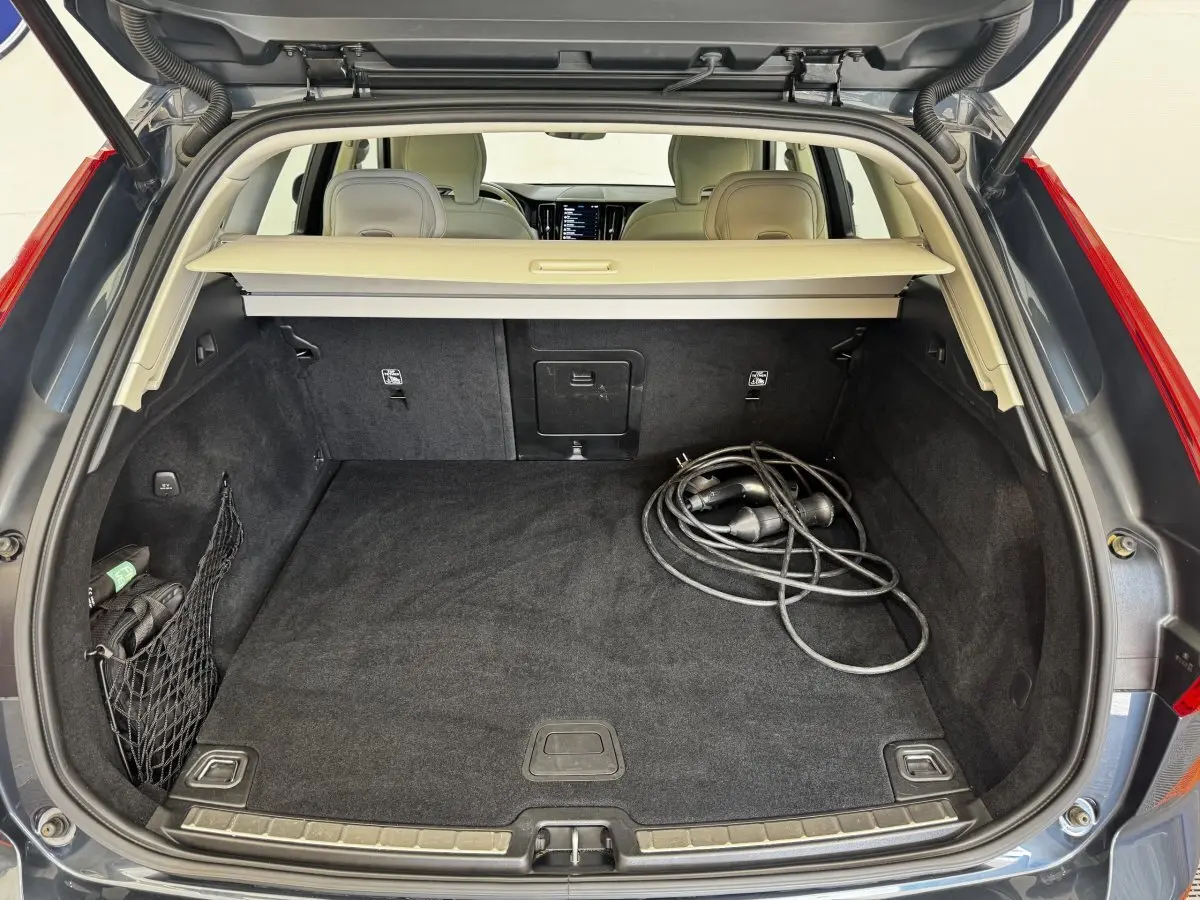Coffre ouvert vu de l'arrière d'un Volvo XC60 bleu, avec câble de recharge hybride visible sur le tapis noir.