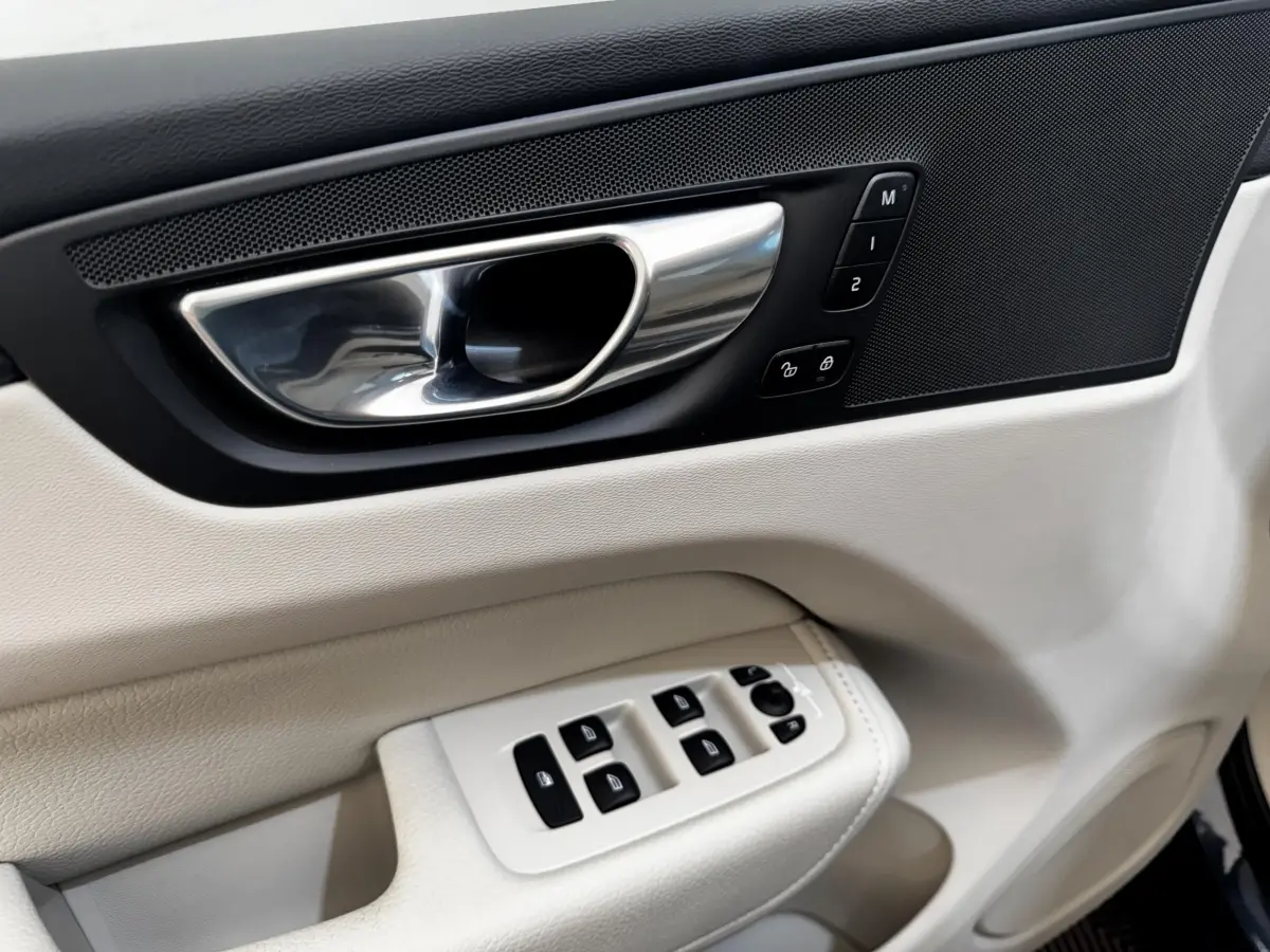 Détail de la porte avant gauche intérieure beige du Volvo XC60 avec commandes de vitres et poignée chrome.