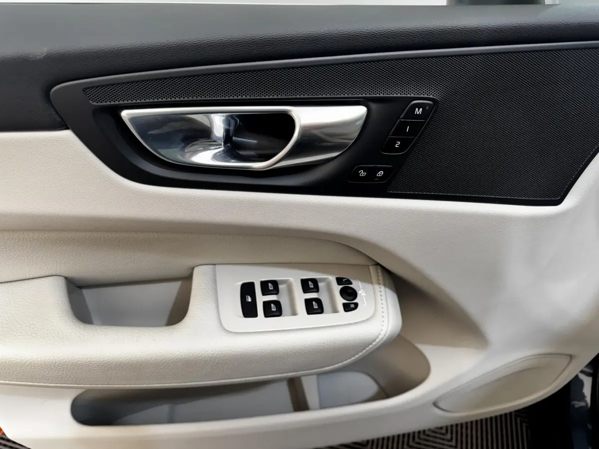 Détail de la porte côté conducteur du Volvo XC60 bleu 2021, avec commandes de vitres et poignée chrome.