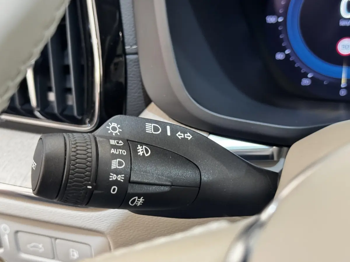 Gros plan sur la commande des phares et clignotants du tableau de bord beige du Volvo XC60 bleu hybride rechargeable.