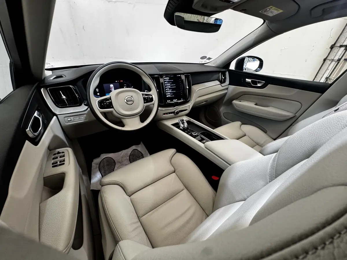 Intérieur beige clair du Volvo XC60 Recharge T8 vu côté conducteur, avec tableau de bord numérique et écran tactile central.