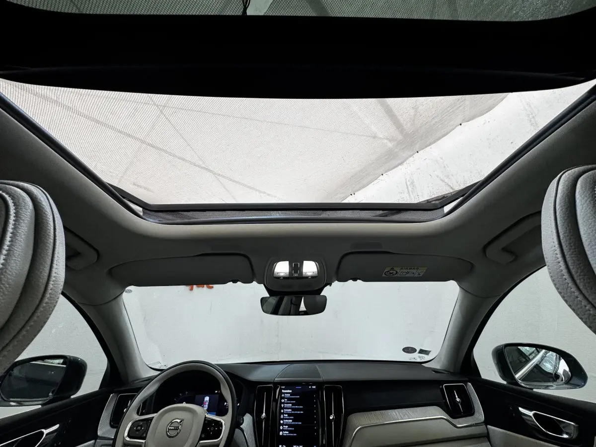 Vue intérieure avant du Volvo XC60 bleu, montrant le toit ouvrant panoramique et le tableau de bord moderne noir et beige.