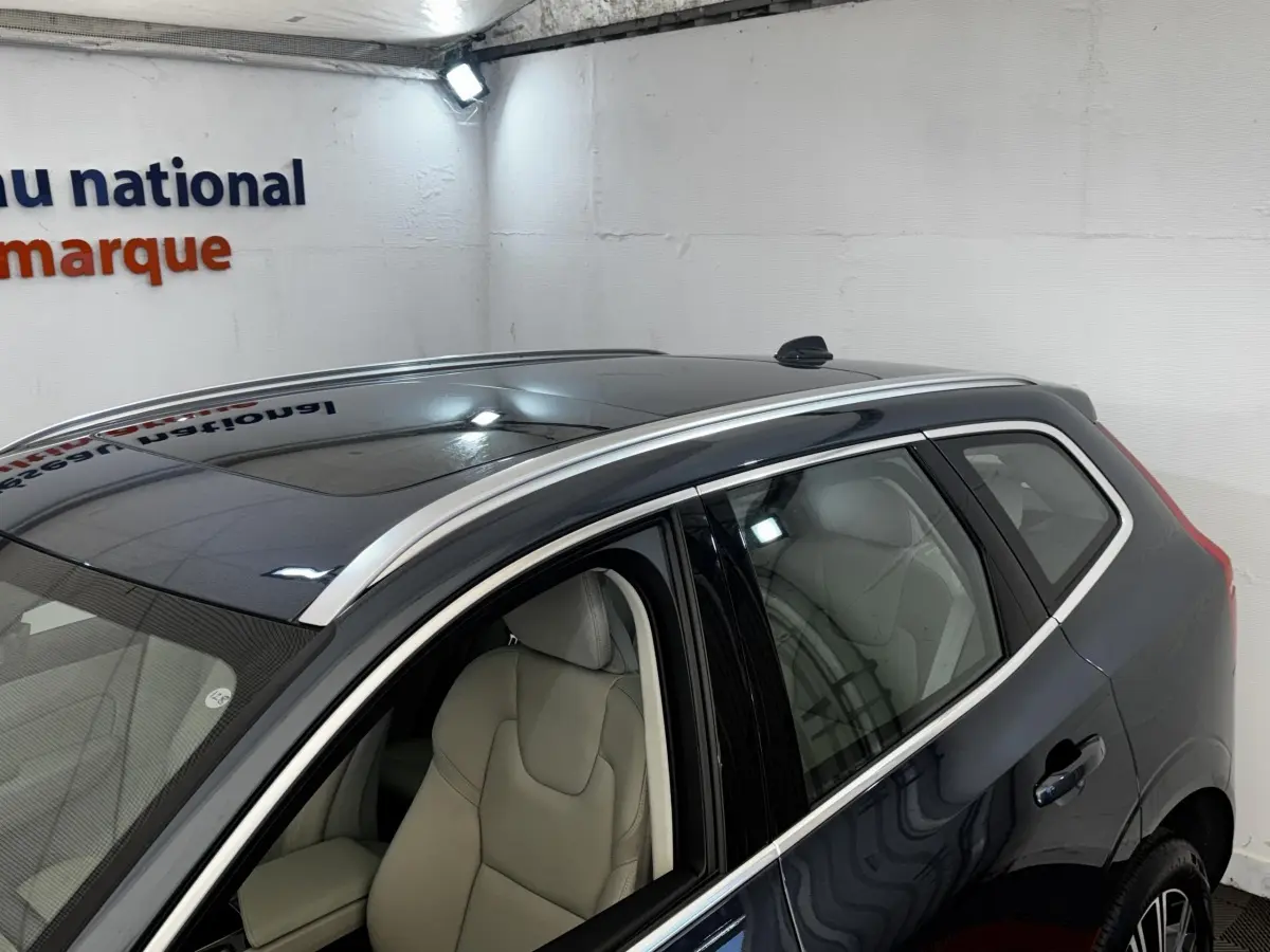 Vue 3/4 arrière droite d’un Volvo XC60 bleu avec toit ouvrant et sellerie claire visible à l’intérieur.