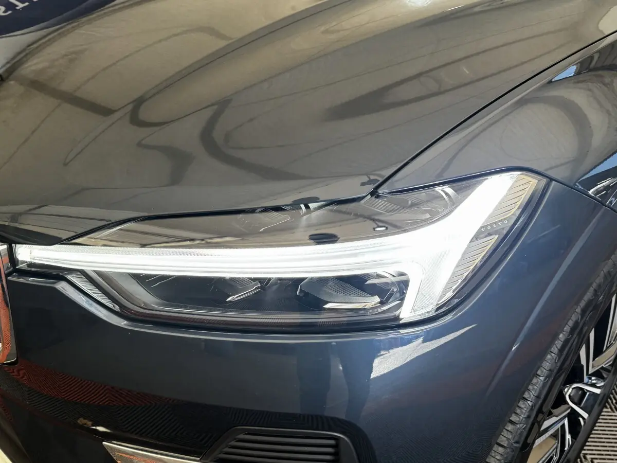 Gros plan sur le phare avant droit allumé d’un Volvo XC60 bleu hybride rechargeable, soulignant ses lignes modernes.