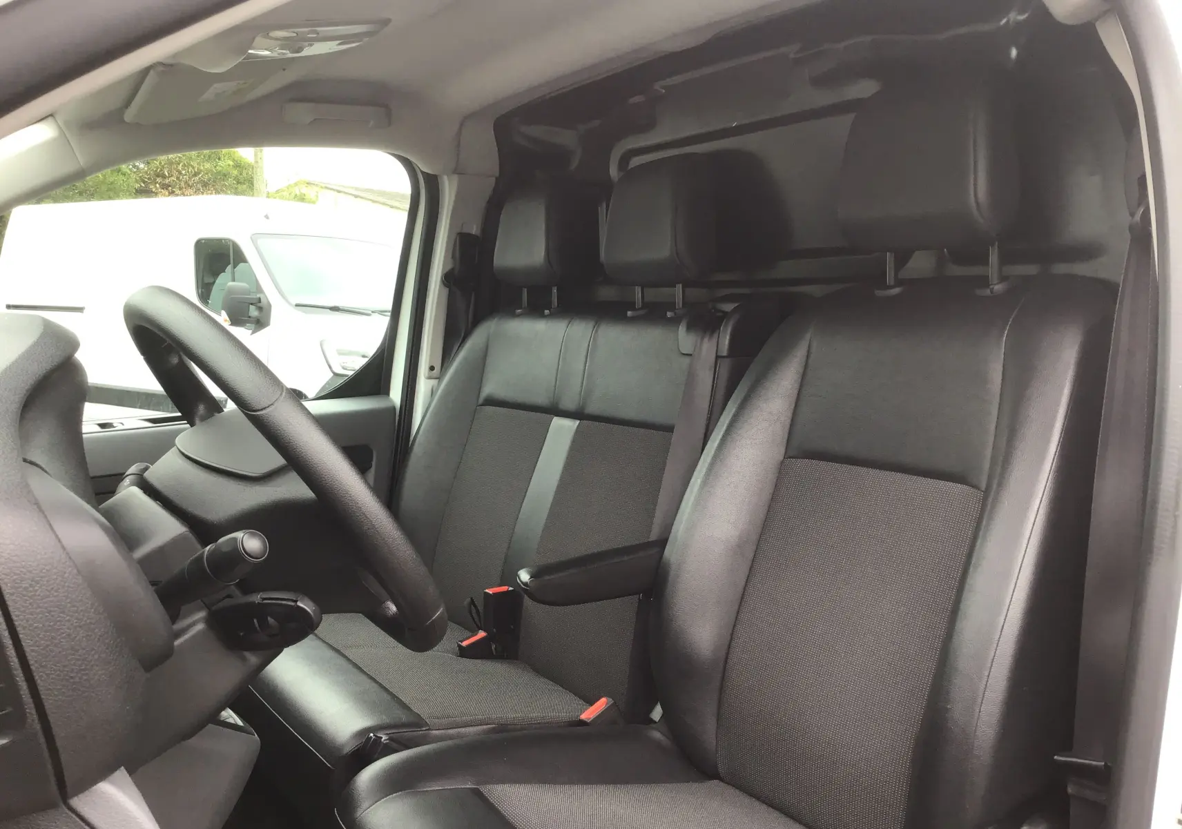 Vue intérieure côté conducteur de l'Opel Vivaro blanc 2022, sièges noirs en cuir et tissu avec accoudoir central.