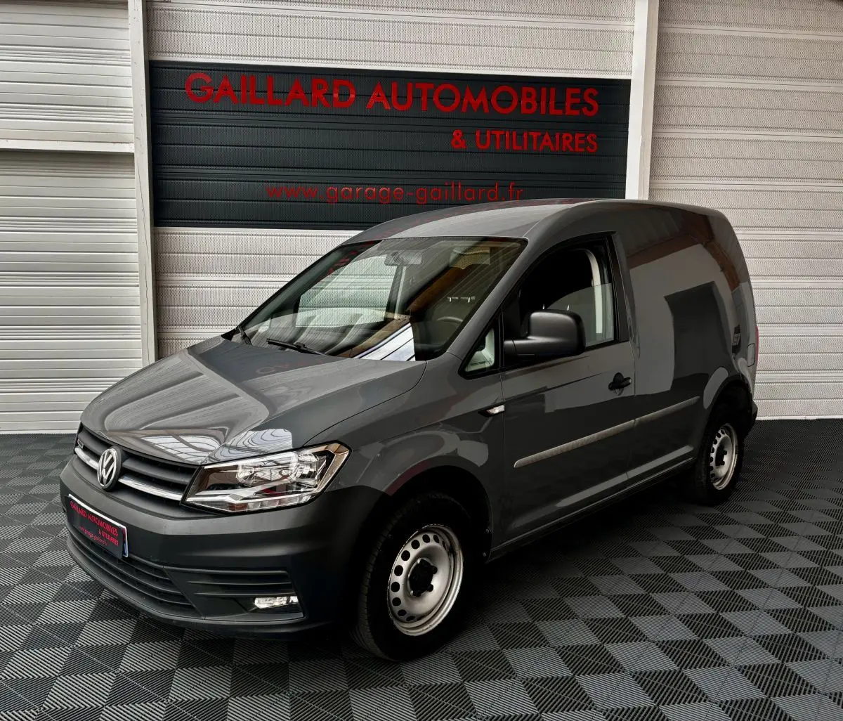 Vue 3/4 avant d'un utilitaire Volkswagen Caddy gris foncé avec calandre noire et jantes acier simples.