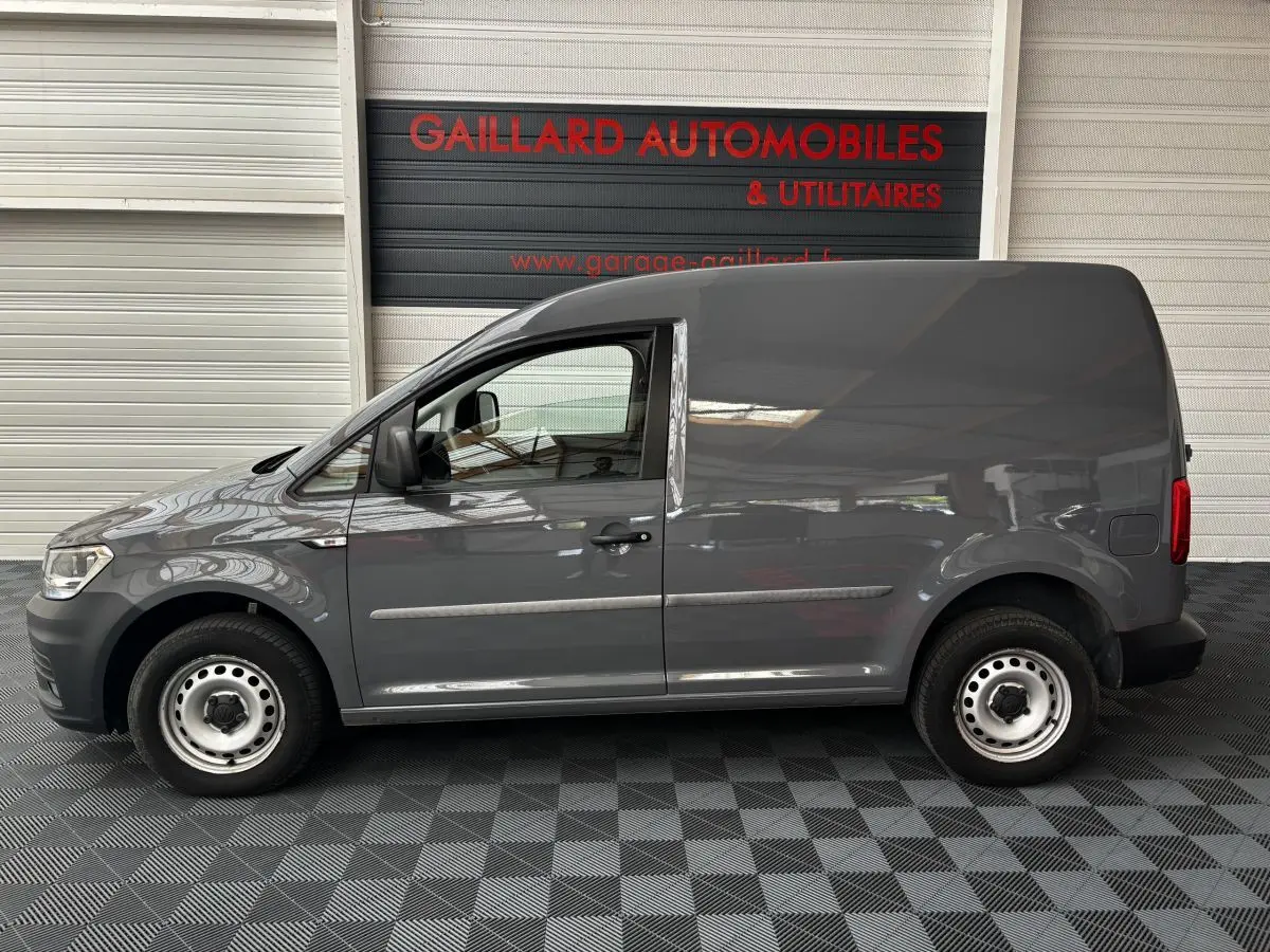 Profil côté gauche d'un utilitaire Volkswagen Caddy gris foncé 2019 avec porte latérale pleine et jantes acier simples.