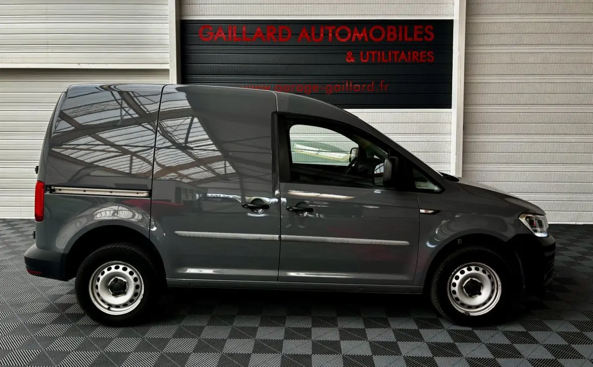 Profil côté gauche d'un utilitaire Volkswagen Caddy gris foncé 2019 avec portes coulissantes et jantes acier simples.