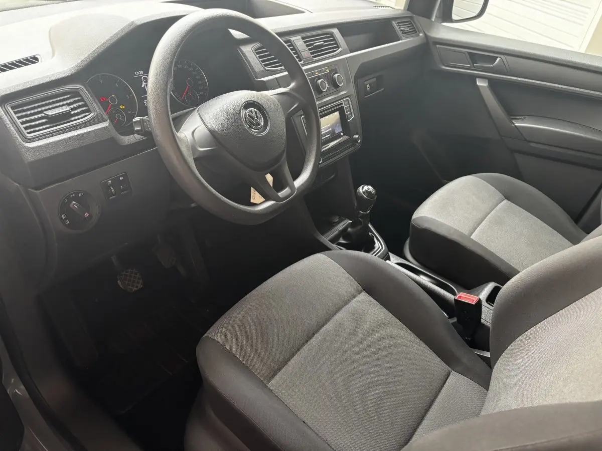 Intérieur avant gris du Volkswagen Caddy 2019, vue côté conducteur avec volant, tableau de bord et boîte manuelle visibles.