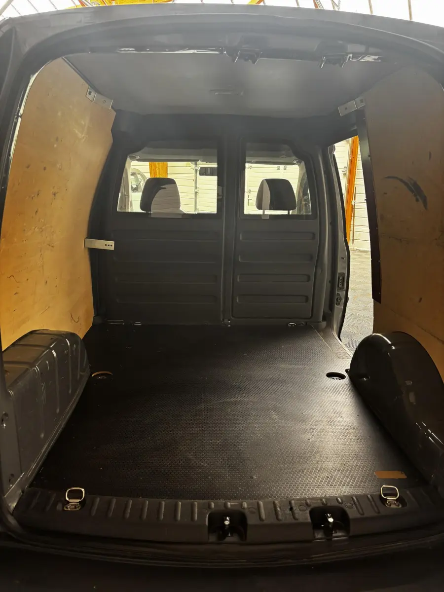 Vue intérieure arrière du Volkswagen Caddy gris foncé 2019, montrant l'espace de chargement avec cloison pleine en bois.