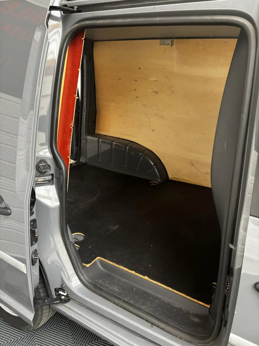 Vue intérieure côté droit de la zone de chargement d'un Volkswagen Caddy gris foncé avec cloison en bois et sol noir antidérapant.