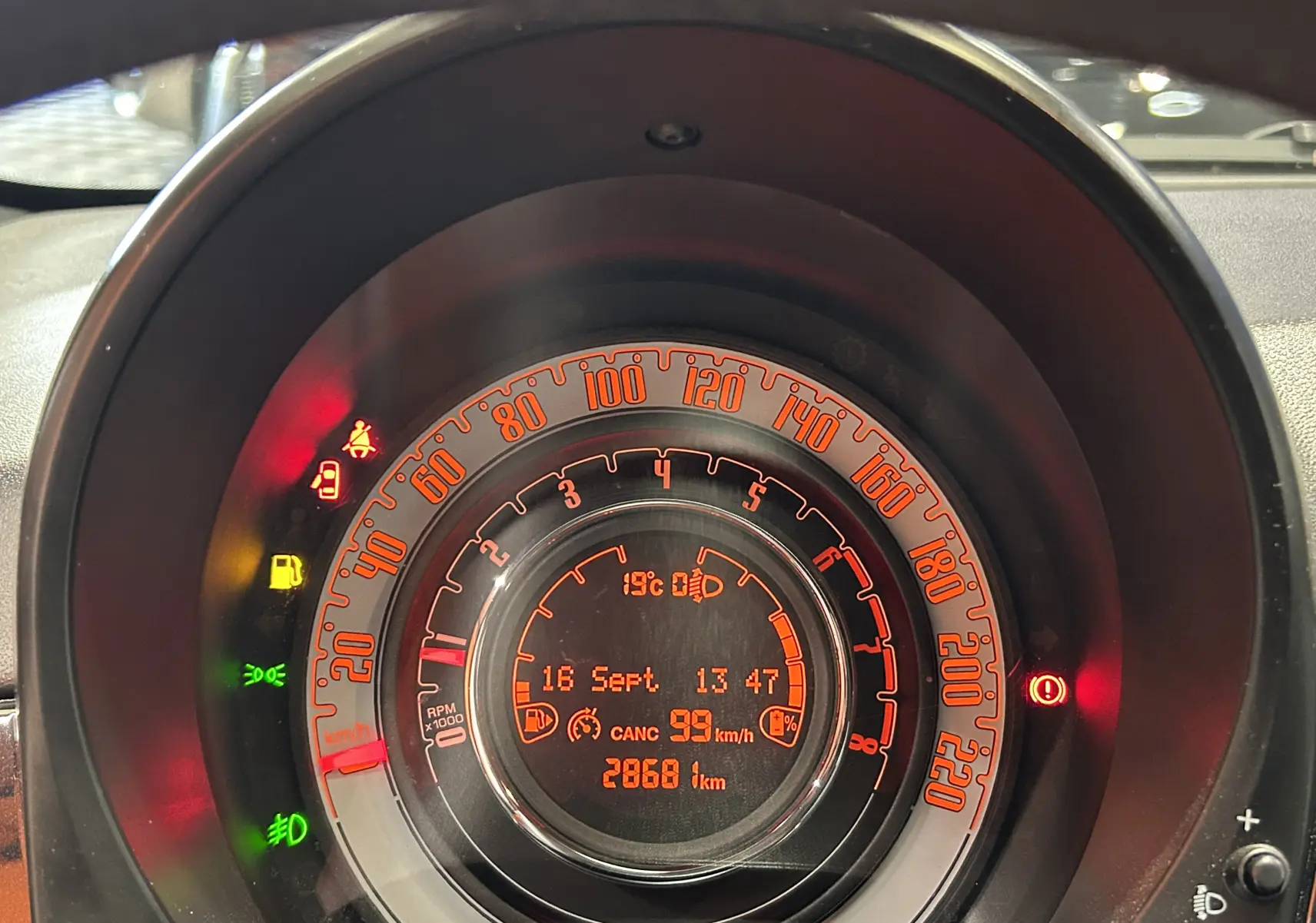 Gros plan sur le compteur orange de la FIAT 500 noire, affichant la vitesse, le compte-tours et les témoins lumineux.