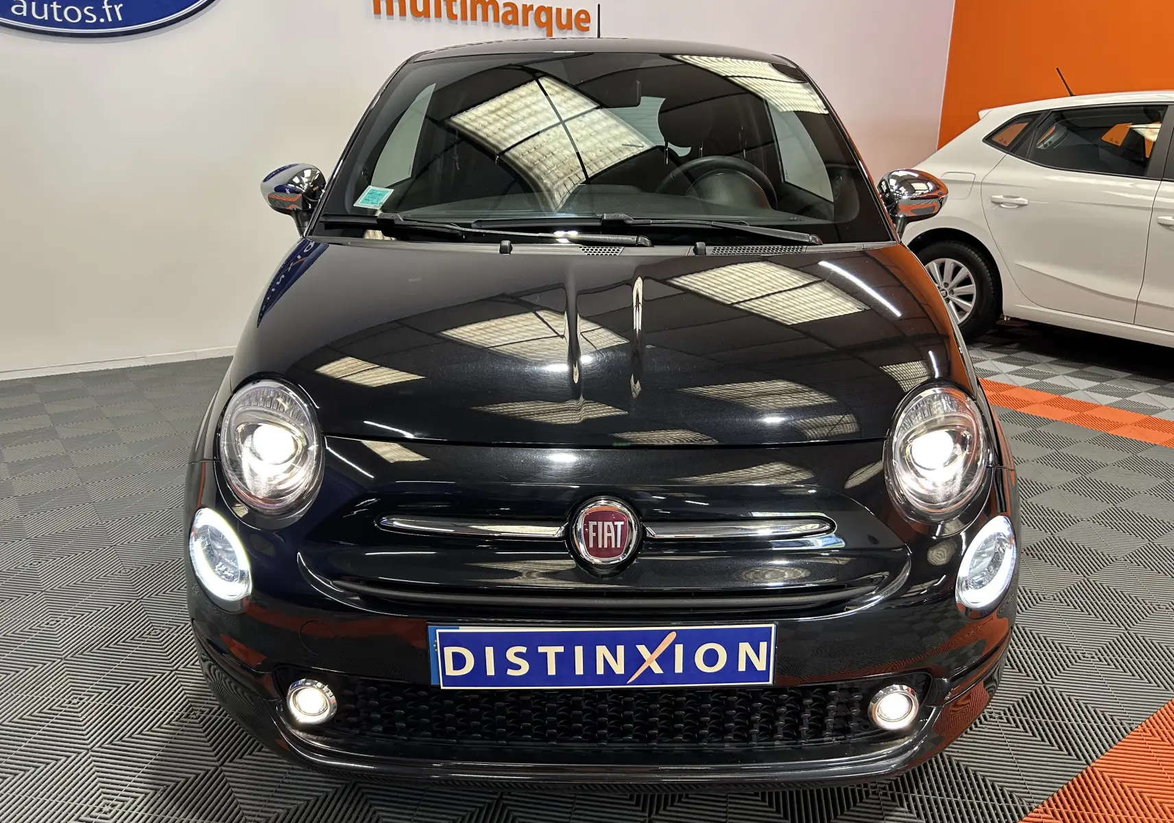 Vue frontale d'une FIAT 500 noire 2023 avec phares allumés et plaque Distinxion en concession multimarque.