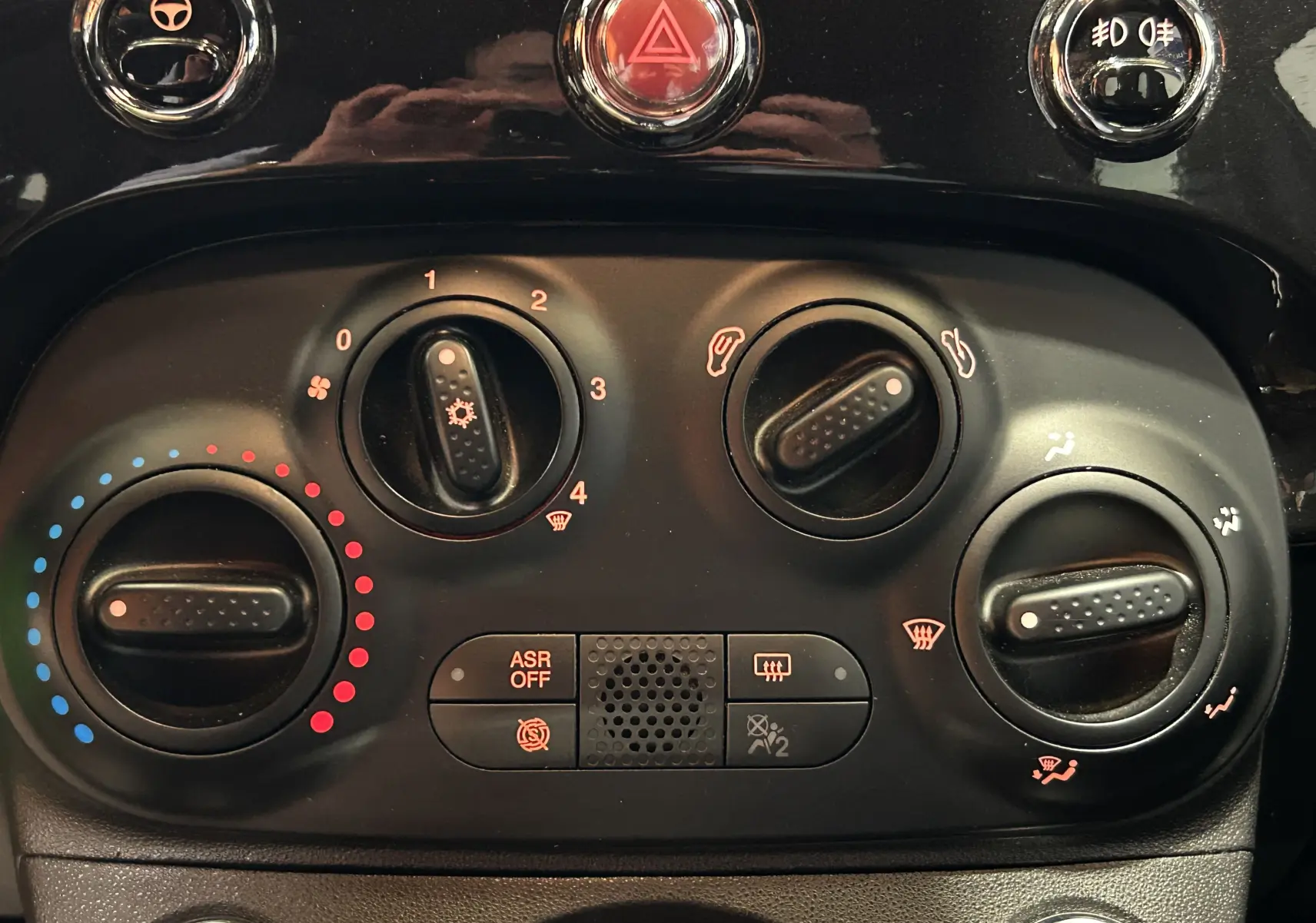 Gros plan sur les commandes de climatisation et sécurité du tableau de bord noir de la Fiat 500 2023 finition Pack Confort.