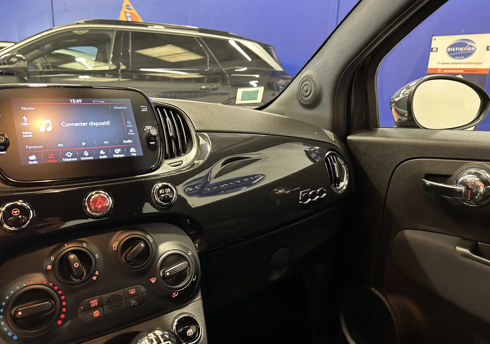 Intérieur côté passager de la Fiat 500 noire 2023, tableau de bord brillant avec logo 500 et écran tactile allumé.