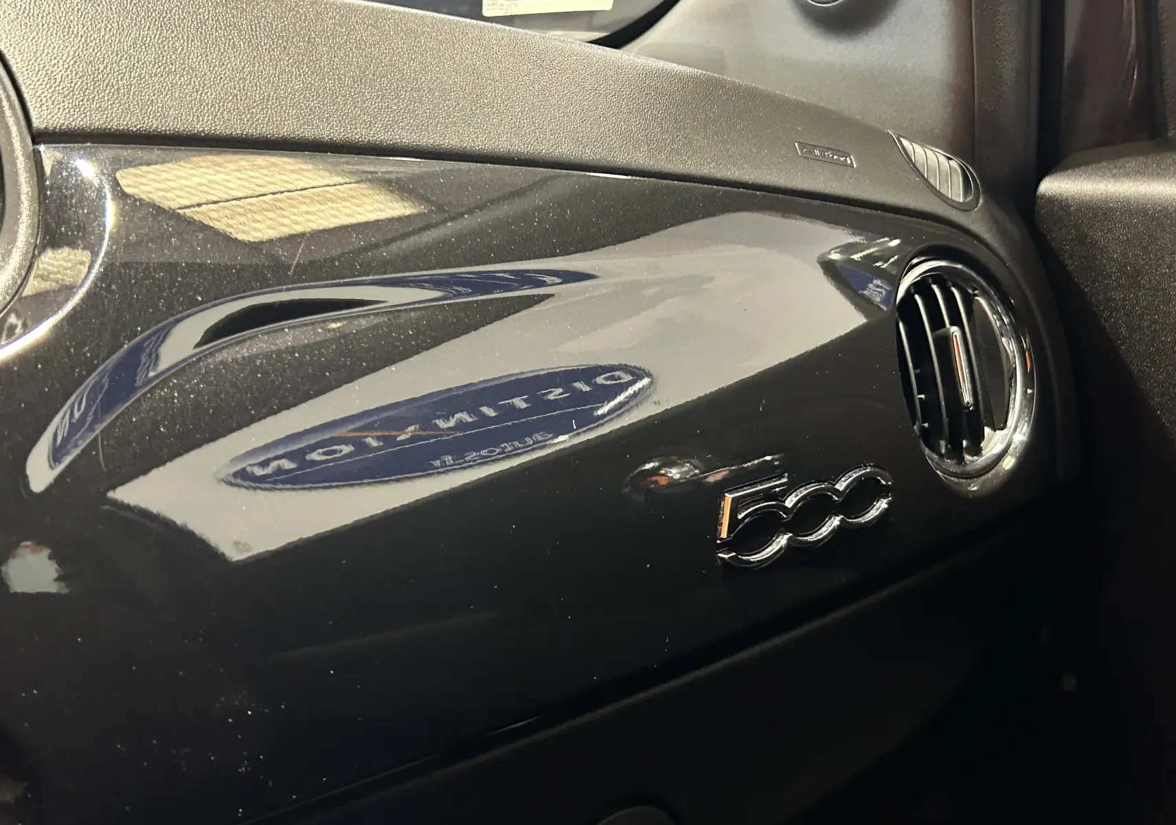 Tableau de bord noir brillant de la Fiat 500 2023 avec logo 500 et sortie d'air ronde côté passager.