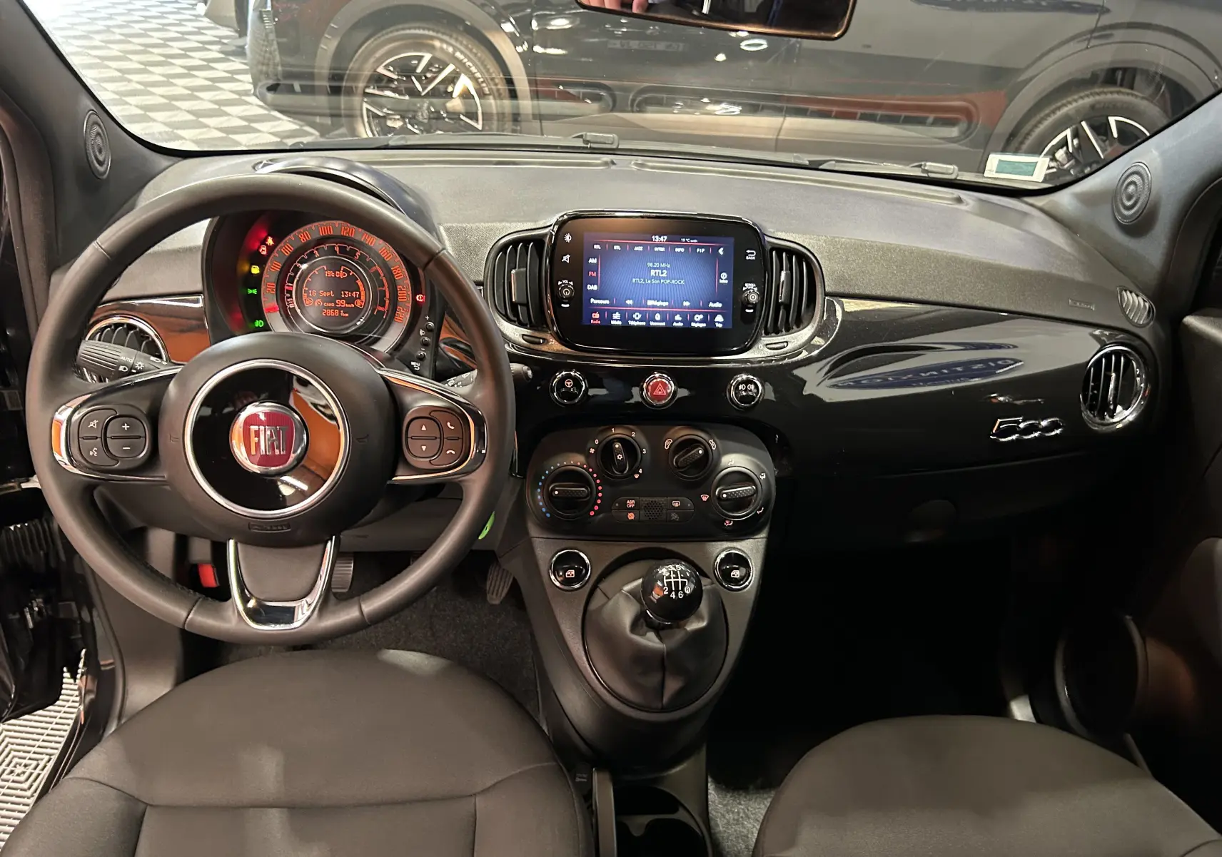 Vue intérieure avant de la Fiat 500 noire 2023, tableau de bord avec écran tactile et volant multifonction.