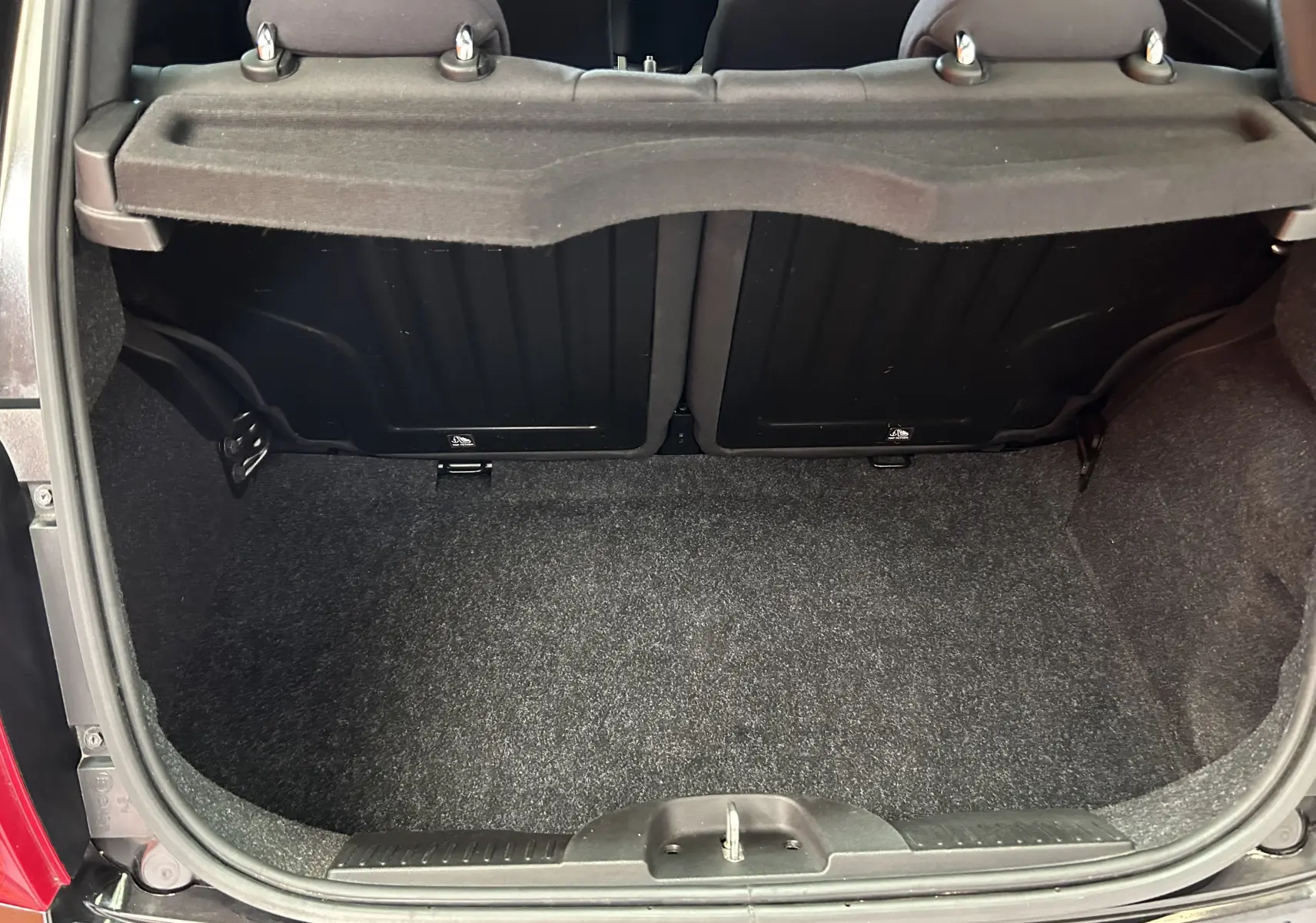 Coffre ouvert vu de l'arrière d'une Fiat 500 noire 2023, montrant l'espace de chargement vide et les dossiers arrière.