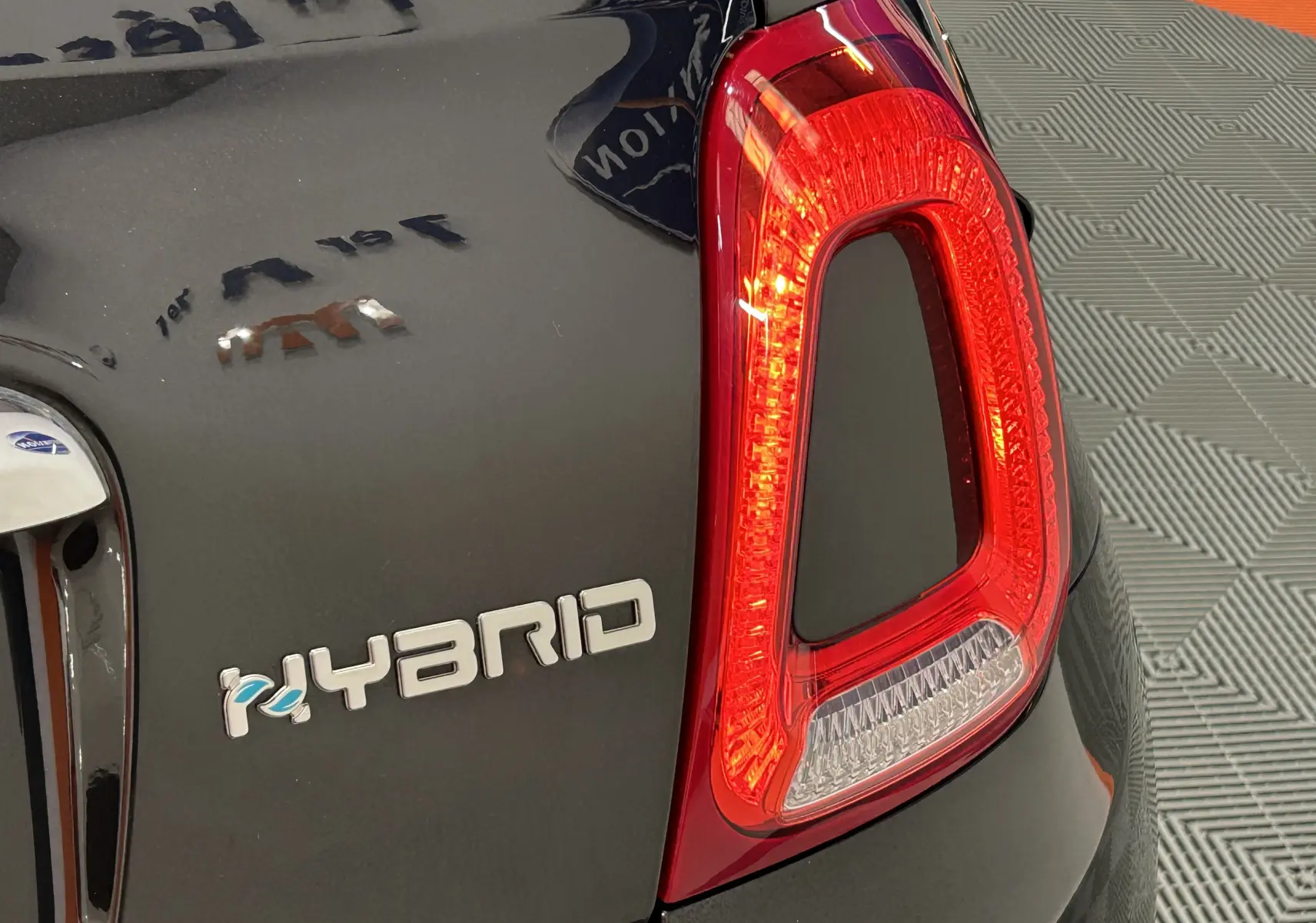 Gros plan sur le feu arrière droit et l'inscription Hybrid d'une FIAT 500 noire 2023 en intérieur.