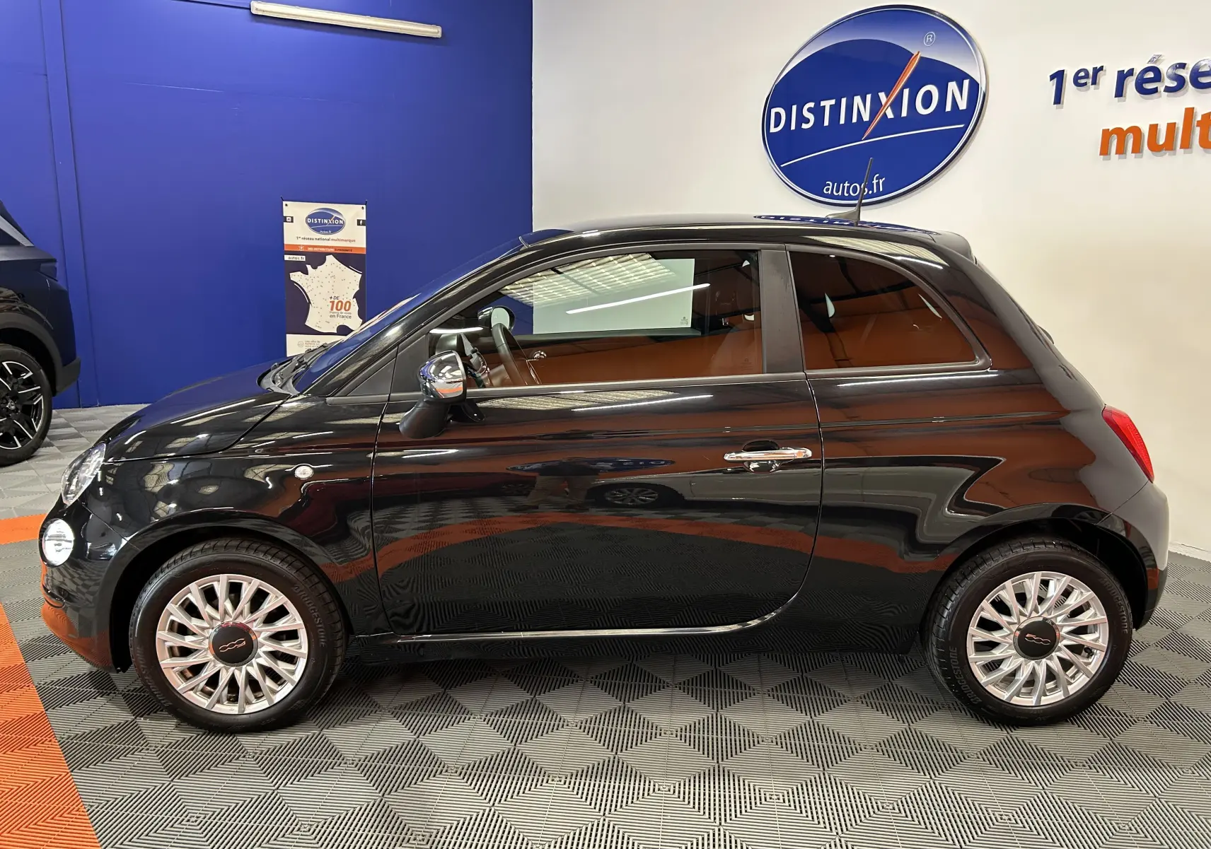 Profil côté gauche d'une FIAT 500 noire 2023 en intérieur, mettant en valeur ses jantes élégantes et sa silhouette compacte.