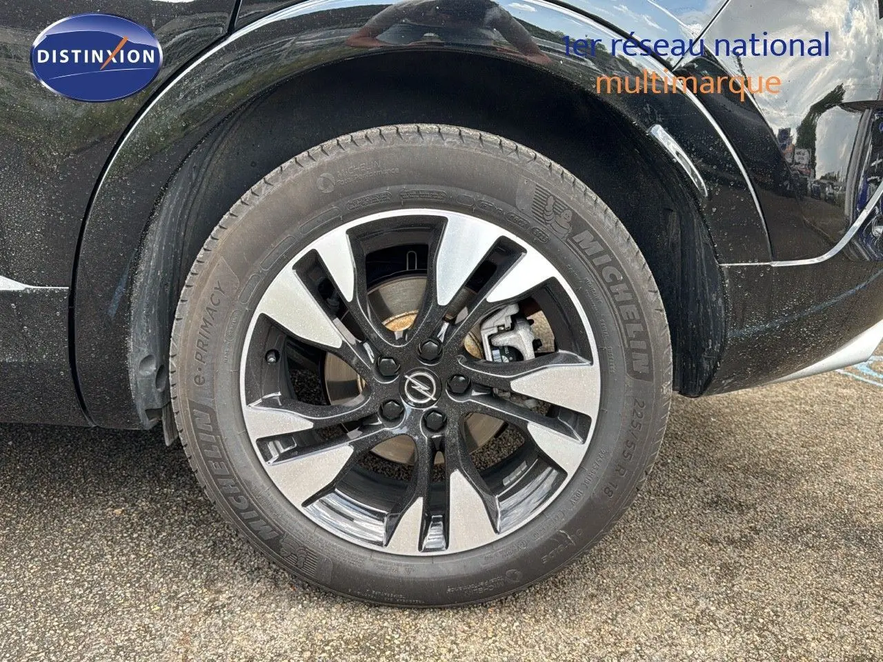 Gros plan sur la roue avant droite noire de l'Opel Grandland 1.6 Turbo Hybrid 225ch GS avec jante bi-ton et logo Opel.