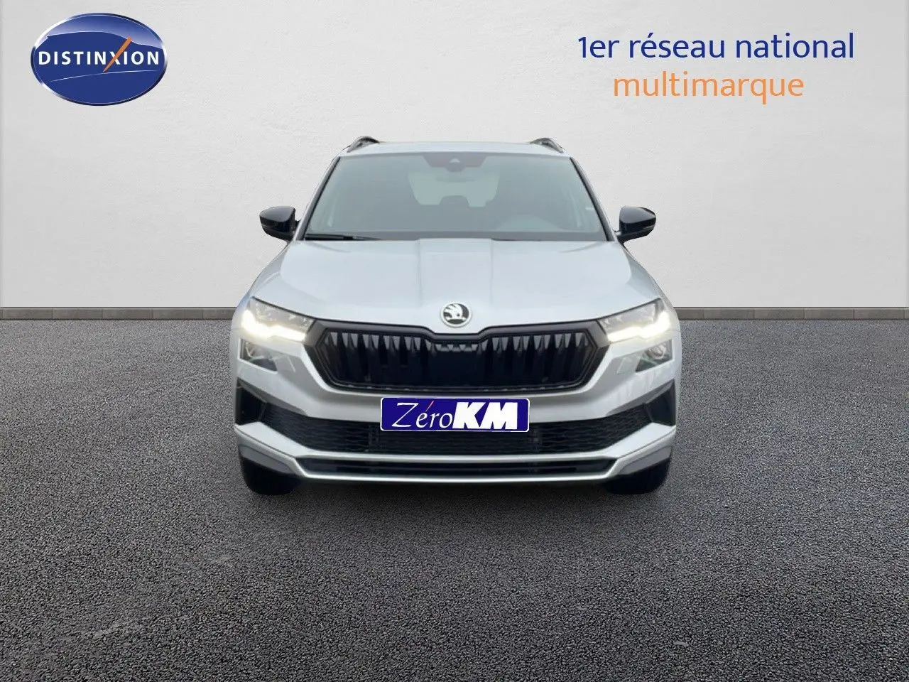 Vue frontale d'un Skoda Karoq gris argent métallisé 2025 avec calandre noire et phares allumés.