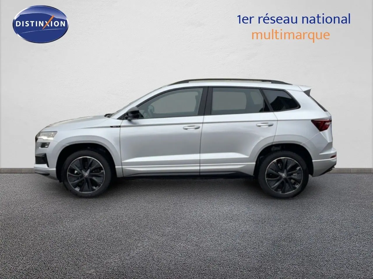 Vue latérale droite d'un Skoda Karoq gris argent métallisé 2025 avec jantes noires et toit ouvrant.