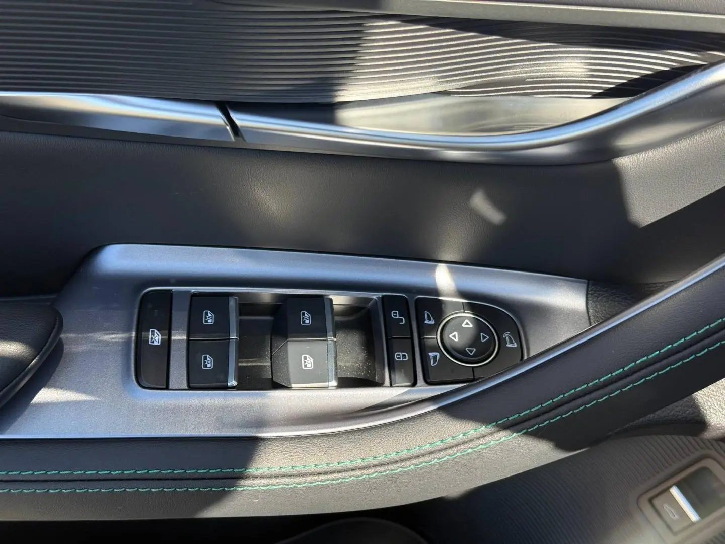 Gros plan sur la commande des vitres électriques côté conducteur du BYD SEAL U 1.5 DM-i en intérieur noir avec surpiqûres vertes.