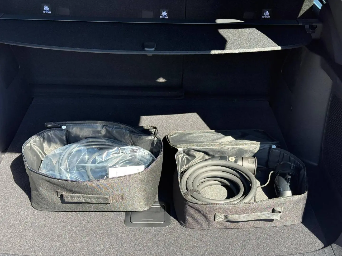 Coffre ouvert du BYD SEAL U 1.5 DM-i 218ch Boost 2026, montrant les câbles de recharge rangés dans des sacs noirs.