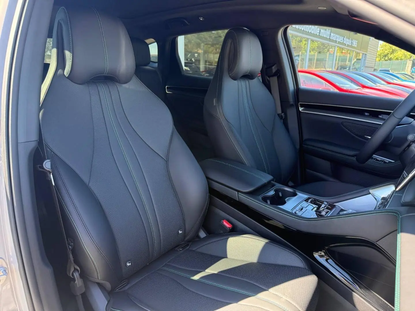 Vue intérieure avant du BYD SEAL U 1.5 DM-i 218ch Boost, sièges cuir noirs avec surpiqûres vertes et console centrale élégante.