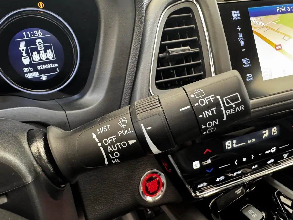 Gros plan sur la commande d’essuie-glace du tableau de bord noir du Honda HR-V blanc, avec écran tactile et bouton start rouge.