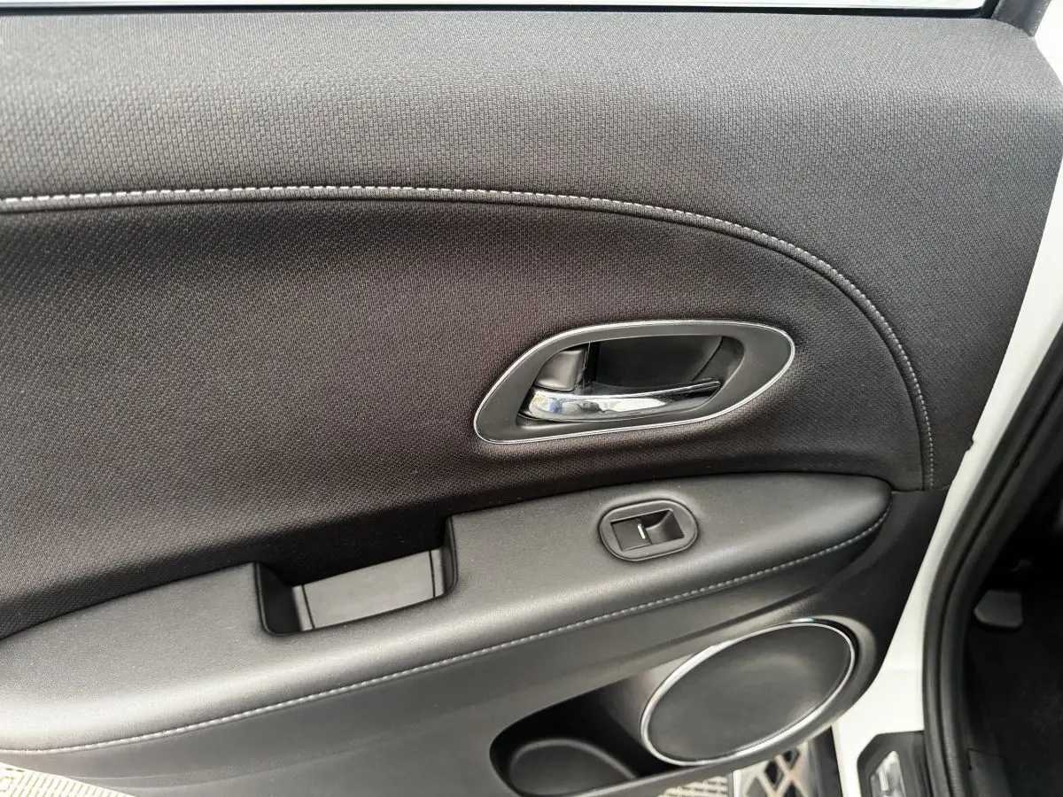 Intérieur de la porte arrière droite noire du Honda HR-V blanc, avec poignée chromée et commande de vitre.