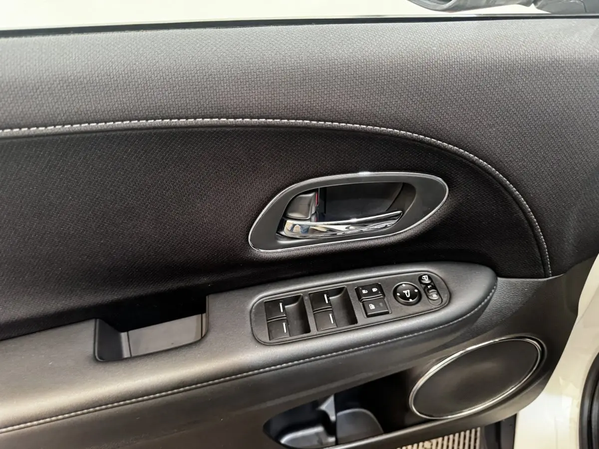 Gros plan sur la porte avant gauche noire avec commandes électriques et poignée chrome d’un Honda HR-V blanc.