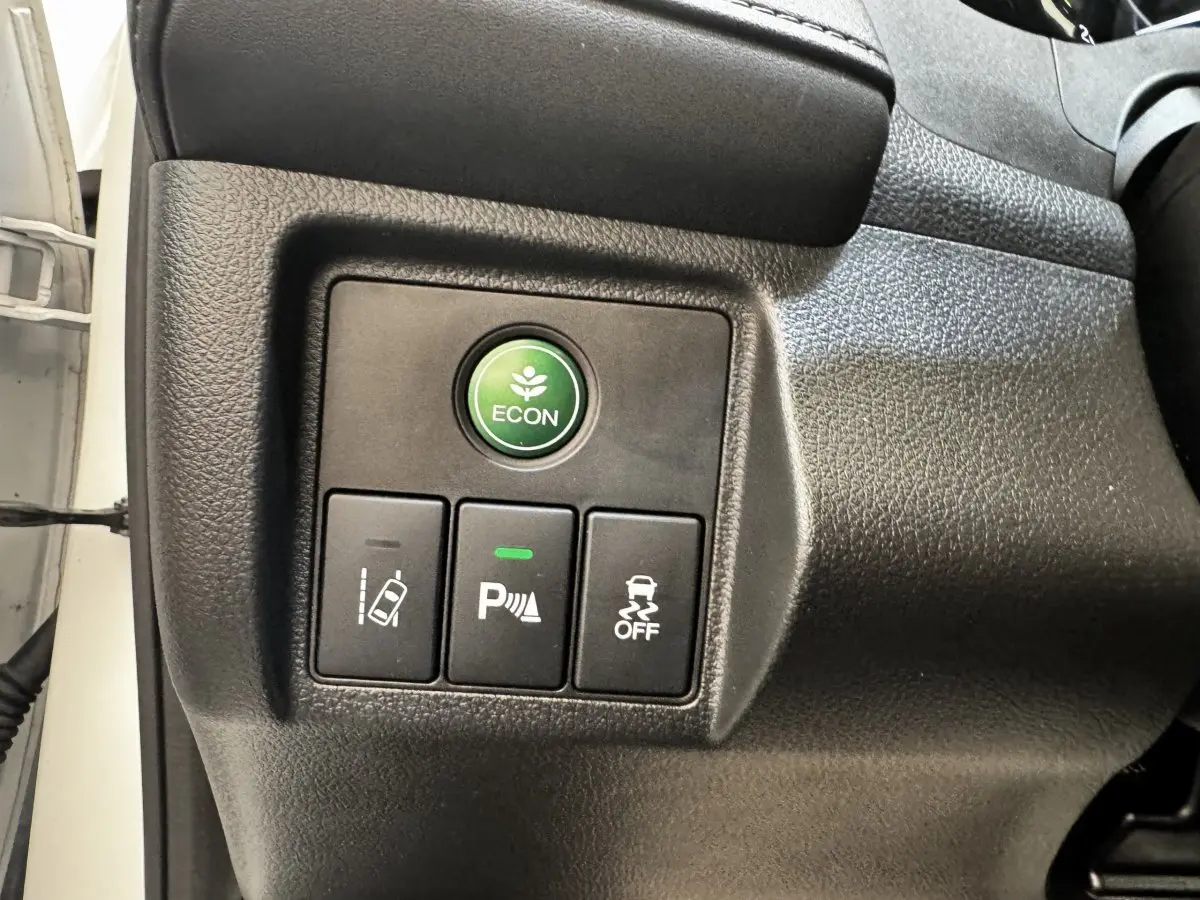 Gros plan sur les boutons de commande du tableau de bord du Honda HR-V blanc, avec bouton ECON vert et aides à la conduite.