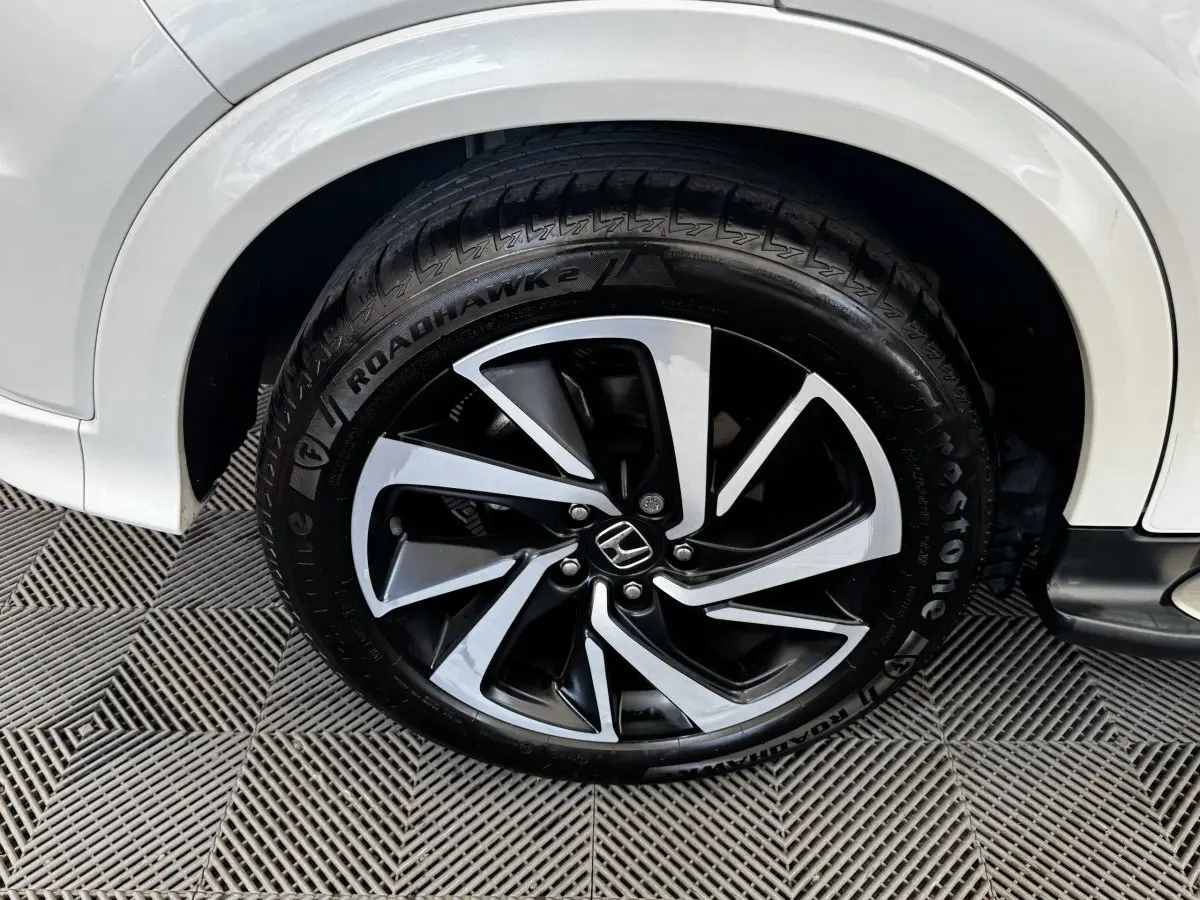 Gros plan sur la roue avant droite d’un Honda HR-V blanc, jante alliage noire et argentée avec logo Honda central.